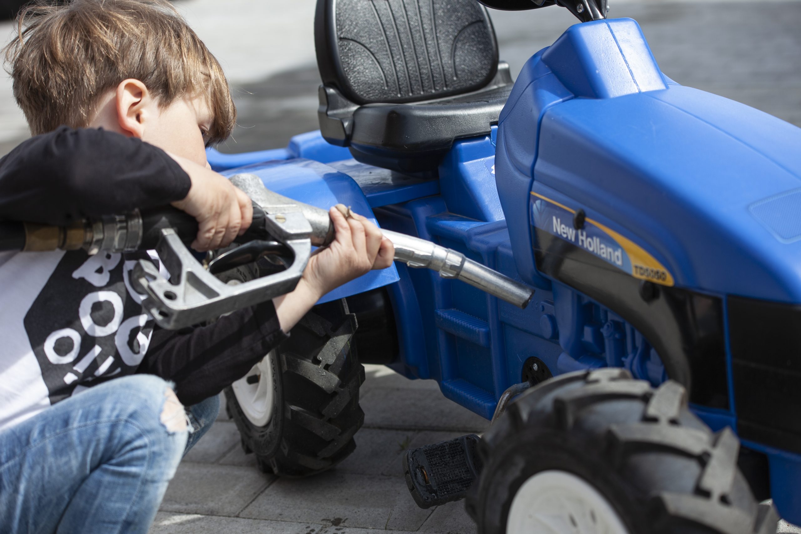 Gutt fyller drivstoff på en leketraktor i parken.