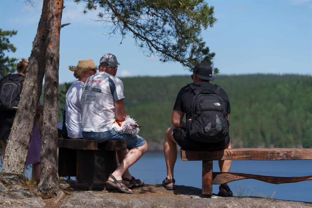 Tre voksne som sitter på benk og ser utover Toke vannet.